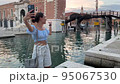 funny energetic woman makes video call using mobile internet on her smartphone. she is a tourist walking around Venice in Italy and posing against the backdrop of the Arsenal 95067530