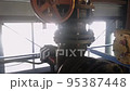 An old valve with a yellow round steering wheel on a heating pipe in a boiler room. 95387448