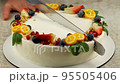 The chef cuts with a serrated knife a homemade carrot-orange cake, decorated with kumquat, pomegranate seeds, blueberries, strawberry slices and fresh mint leaves. Diet healthy cake, without sugar and 95505406