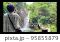A woman taking a picture of a waterfall on the walking path of Shosenkyo Gorge 95855879
