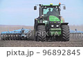 Modern red tractor plows an agricultural field 96892845