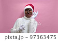 A man is dancing wearing a mask for Halloween, a santa hat on a pink background 97363475