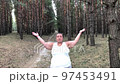 A fat woman is engaged in breathing exercises in a pine forest. Mental health. Gray hair 97453491