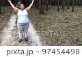 A fat woman is engaged in breathing exercises in a pine forest. Mental health. Gray hair 97454498