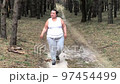 A fat woman is engaged in breathing exercises in a pine forest. Mental health. Gray hair 97454499