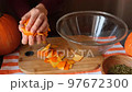 a woman puts pumpkin peelings into a large glass bowl with her hands 97672300