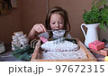 a little girl sprinkles powdered sugar on a Christmas stollen while sitting at the kitchen table. 97672315