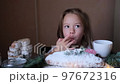 a little girl tries powdered sugar with her finger from a Christmas stollen while sitting at the table 97672316