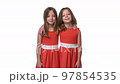 Two smiling pre-teen twin girls standing hugging while looking at camera 97854535