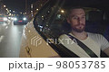 Bearded young man is sitting in the passenger seat going by taxi in the night 98053785