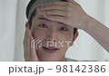 Skin care image A young man looking at the camera holding his cheeks, forehead and chin 98142386