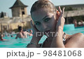 Sweet woman in swimsuit straightening hair, posing in outdoor swimming pool  98481068