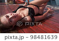 Pretty young girl in swimming suit lying on wooden deck, relaxing and sunbathing 98481639