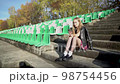 Young blonde girl is sitting on steps on the empty football stadium, 98754456