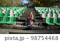Young blonde girl is sitting on steps on the empty football stadium, 98754468