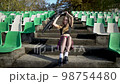 Young blonde girl is sitting on steps on the empty football stadium, 98754480