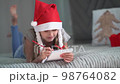 Christmas miracle wish list. Smiling girl in Santa Claus hat writing letter 98764082