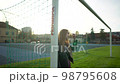 Blonde woman in skirt and lather jacket stands near soccer net at sport field 98795608