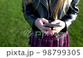 Close-up view of girl using mobile phone at park, Lather jacket, skirt 98799305