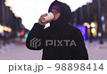 Young handsome man in glasses is walking in city in winter, drinking hot tea or coffee from paper cup 98898414
