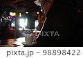 Young handsome man drinks hot coffee cup on a wooden table and uses mobile phone. Hot Coffee Drink Concept. 98898422