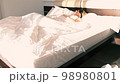 Waking up, sleeping. Young woman with blindfold wakes up in bed from the sun's rays filling the room. The girl rolls over on her back and removes the blindfold from her eyes. 98980801
