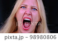 Woman screams in rage with her mouth wide open staring at camera. Aggression, indignation. Close-up headshot of blue-eyed blonde experiencing an overabundance of emotions. Hysteria, screaming 98980806