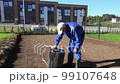 Worker man screw bolt of roller filled with water with spanner tool. Preparing equipment for compacting soil in yard. Lawn seeding stage. Static shot 99107648