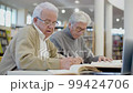 Focused senior men writing abstract in notebook in library 99424706
