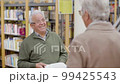 Cheerful senior man discussing book with friend in library 99425543
