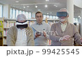 Senior men using virtual reality glasses with teacher in library 99425545