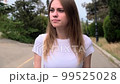 Beautiful and confident, outdoor smiling portrait of a relaxed young woman walking along the alley of the park along the trees. Daily walk in the fresh air. 99525028