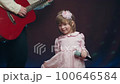 Little girl on stage in vintage dress, she sings into microphone and dances, her father plays acoustic guitar. Color music is shining. Performance on stage. Early development of children 100646584