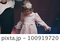 Little girl on stage in pink vintage dress, she dances, her father plays acoustic guitar. Color music is shining. Performance on stage. Early development of children 100919720