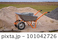 Putting sand with a shovel or spade outdoors into metallic buckets standing on a hand cart 101042726