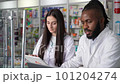 4K high quality footage of a dark-skinned male and young female pharmacy professionals working on laptop computer and digital tablet in a drugstore. A teamwork approach to quality healthcare services 101204274