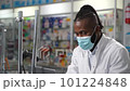 A portrait of a male black pharmacist in a protective face mask, welcoming and assisting a female customer in a retail drugstore to buy prescription drugs, captured in high-quality 4K footage 101224848