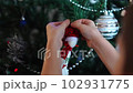 The hands of a child decorating an artificial Christmas tree with a toy in the form of a snowman. The atmosphere of preparation for the holiday. 102931775