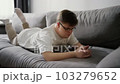 Young man with down syndrome using cellphone while resting on couch at home 103279652