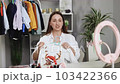 Young lady fashion designer using mobile phone receiving purchase order and showing clothes recording video live streaming online at shop. Small business owner, online market delivery concept 103422366