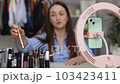 Female beauty blogger social media influencer talking on smartphone camera, recording vlog, broadcasting social media, making video call at home. Cosmetics shopping haul or makeup unpacking on cell 103423411