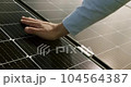 Zoom in tracking shot of anonymous male engineer in shirt touching surface of photovoltaic panel at sunset. Technician connecting solar panel. Crop man touching solar panel. 104564387