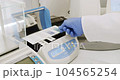 Crop scientist spreading colored sample on glass. From above anonymous scientist in latex gloves spreading blue liquid on glass on white table during work in laboratory 104565254
