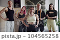Confident sportspeople in gym together. Handheld shot of team of self assured male and female athletes in sportswear looking at camera while standing in light studio before training. 104565258