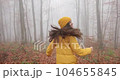 An attractive young woman in bright yellow clothes with long dark hair is running in the autumn forest. A woman feels happy in nature. Autumn forest. 104655845