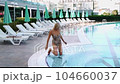Portrait of happy mature adult woman relaxing deck chair near the pool while looking at camera. Beautiful smiling caucasian senior woman in hat enjoying summer vacation 104660037