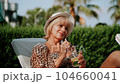 Portrait of happy mature adult woman in hat relaxing deck chair near the pool. Beautiful elegant caucasian senior woman in sunglasses drink lemonade cocktail enjoying summer vacation 104660041