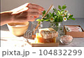 Natural bathroom and home spa tools. Zero waste sustainable lifestyle concept. Woman hands with Bamboo toothbrush, tooth powder, soap bar, cotton pads, swabs, flowers on white background. Front view. 104832299