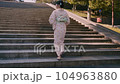 A woman in a yukata walking up the stone stairs of a temple 104963880