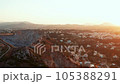 Aerial view sunrise over village on Greek island, hilly area geological formations, early morning or evening golden hour, rural scene drone flies above coastal town lit with warm sunlight 105388291